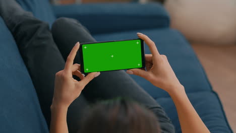 Freelancer-sitting-on-sofa-while-looking-at-movies-using-phone-in-horizontal-mode-with-mock-up-green-screen