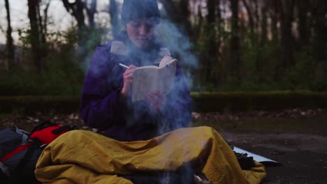Young-female-backpacker-making-notes-at-campfire