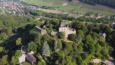 Ruins-of-Badenweiler-castle-atop-forested-hillside-overlooking-spa-town,-aerial