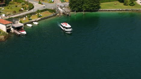 Lake-Orta-in-Pella,-Italy,-ferry-boat-leaving-dock,-aerial-drone-view,-day
