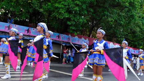 A-group-of-young-girls-wearing-a-colorful-costumes-and-carrying-a-banner-standing-on-the-street-for-the-parade-in-Davao-City,-the-Philippines