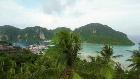 Revealing-drone-shot-of-Phi-Phi-Island-Bay-with-tropical-mountains-during-cloudy-day-above-palm-trees,-Thailand