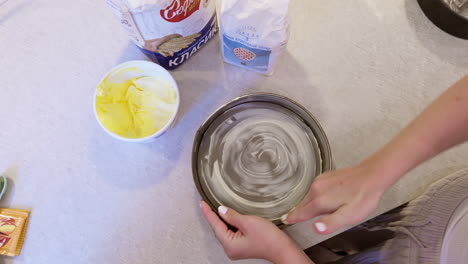 Cake-baker-greases-tin-with-bare-hands-on-kitchen-worktop-top-down-view