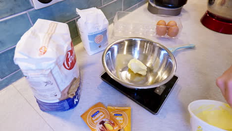 Home-cook-weights-butter-into-mixing-bowl,-while-preparing-to-bake-cakes