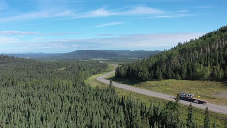 Drone-flies-over-winding-Alaska-Highway-through-lush-boreal-forest