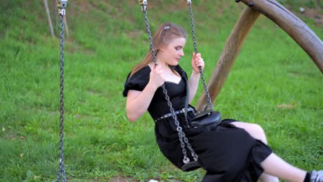 Young-girl-in-a-long-black-dress-is-smiling-while-swinging-on-a-swing