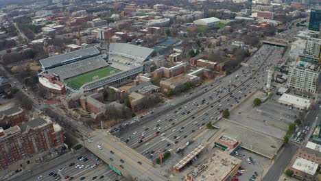 Aerial-drone-shot-flying-backwards-over-a-highway-in-downtown-Atlanta,-Georgia-looking-at-the-campus-of-Georgia-Technical-Institute-and-Bobby-Dodd-Stadium