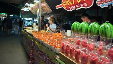 Displays-of-fruits-and-deep-fried-snacks-of-hotdogs-and-barbecue-are-prepared-and-arranged-by-local-vendors-inside-Chatuchak-Night-Market-in-Bangkok,-Thailand