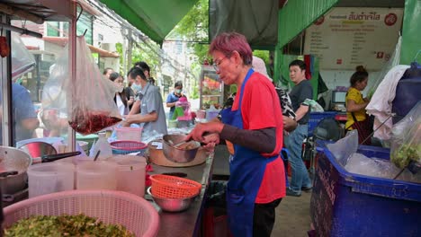 Leyendo-Pedidos-Y-Preparando-Su-Famosa-Comida-Isan-Llamada-Laab,-Esta-Vendedora-Ambulante-Local-Está-Ocupada-Preparando-Los-Pedidos-De-Sus-Clientes-En-Las-Calles-De-Bangkok,-Tailandia