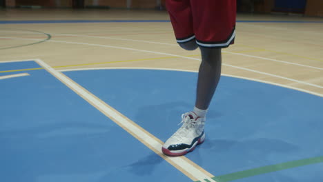 Ein-Basketballsportler-Streckt-Seine-Beine-Mitten-Auf-Einem-Leeren-Spielfeld-Aus-Und-Führt-Vor-Dem-Spiel-Eine-Routine-Durch,-Um-Sich-Fit-Zu-Halten-Und-Sich-Auf-Sein-Bevorstehendes-Spiel-Vorzubereiten