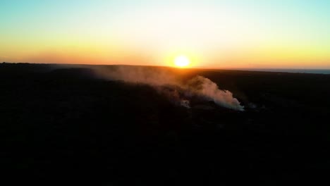 Smoke-rises-across-dark-barren-landscape-as-sun-dips-below-horizon