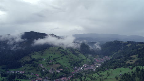 Aerial-view-of-a-mountain-resort-village-located-in-a-valley-surrounded-by-mountains-with-green-fir-forests-and-a-sky-with-very-low-clouds