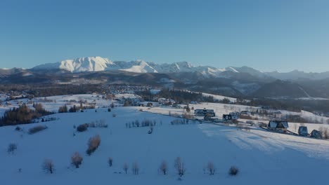 Beautiful-Winter-Panorama-Shot-with-distant-houses,-snowy-mountains-and-snow-covered-panes-of-land