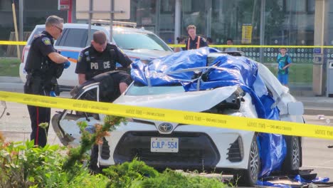Police-officers-looking-inside-of-Crashed-car,-yellow-tape-on-crime-scene,-Brampton