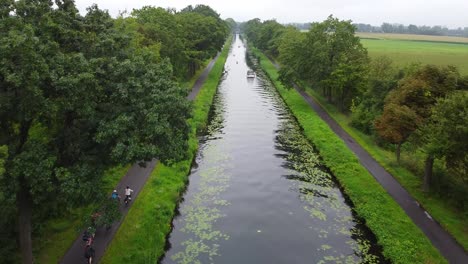 Aerial-view-of-busy-canal-with-kayaks-and-a-boat-crossing,-cyclists-cycling-on-the-bike-lane