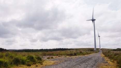 Shot-of-two-wind-turbines-generating-electricity-by-a-dirt-track-road