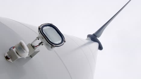 Low-Angle-Aufnahme-Eines-Scheinwerfers,-Der-An-Einer-Windkraftanlage-Befestigt-Ist,-Die-Ihre-Rotorblätter-Dreht