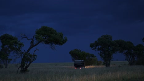 Vehicle-driving-away-at-twilight-on-Night-Safari,-headlights-glowing,-African-nature-in-Maasai-Mara-National-Reserve,-Kenya,-Africa-Safari-adventure-in-Masai-Mara-North-Conservancy