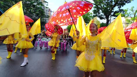 A-group-of-children-in-yellow-dresses-while-holding-red-umbrellas-and-walking-onto-the-parade