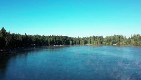 Aerial-pedestal-above-beautiful-blue-lake-water-surrounded-by-thick-conifer-tree-forest