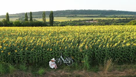 Girl-reads-book-among-sunflowers-in-rural-evening-countryside-pull-shot-reveal