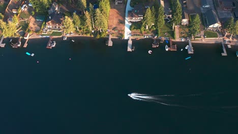 Bird's-eye-view-tracking-pan-follows-boat-driving-along-backyard-docks-in-beautiful-lake,-aerial