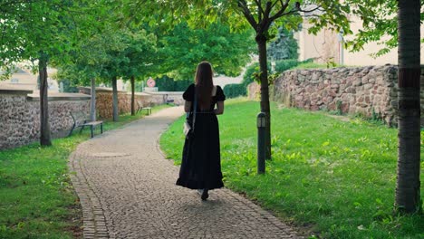 Girl-with-flowing-long-hair-and-a-black-dress-walking-in-a-city-park-on-a-sunny-summer-day