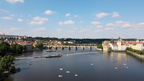 Drone-flying-over-Moldau-river-facing-Charles-Bridge-in-Prague,-Czech-Republic