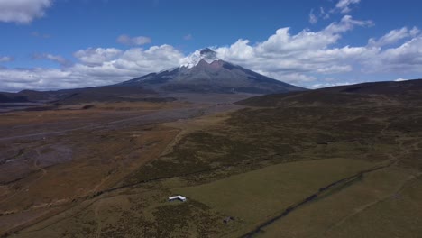 Witness-the-awe-inspiring-Cotopaxi-Volcano-in-4K-as-our-drone-gracefully-retreats,-capturing-the-serene-beauty-of-the-majestic-peak-against-a-backdrop-of-clear-blue-skies-and-gentle-surrounding-clouds