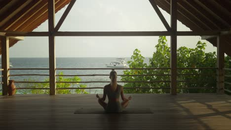 Mujer-Sentada-En-Una-Pose-Fácil-De-Yoga-Meditando-Con-El-Relajante-Sonido-Del-Océano-En-Un-Patio-Privado-Al-Aire-Libre