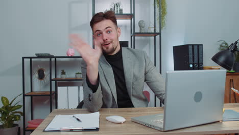 Businessman-working-on-laptop-smiling-friendly-at-camera-and-waving-hands-gesturing-hello-at-office