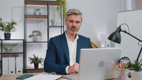 Business-man-working-on-office-laptop-pointing-to-camera-looking-with-happy-expression-making-choice