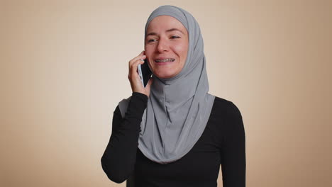 Happy-young-muslim-woman-making-pleasant-mobile-phone-call-conversation-with-good-friend-or-family
