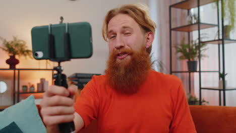 Bearded-man-blogge-taking-selfie-on-smartphone-communicating-video-call-home-online-with-subscribers