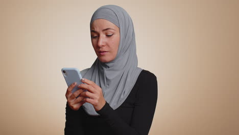 Eine-Glückliche-Muslimische-Frau,-Die-Ihr-Mobiltelefon-Benutzt,-Sagt:-„Wow,-Ja,-Ich-Habe-Herausgefunden,-Dass-Es-Großartige-Nachrichten-über-Einen-Großen-Gewinn-Gibt“,-Indem-Sie-Eine-Siegergeste-Macht
