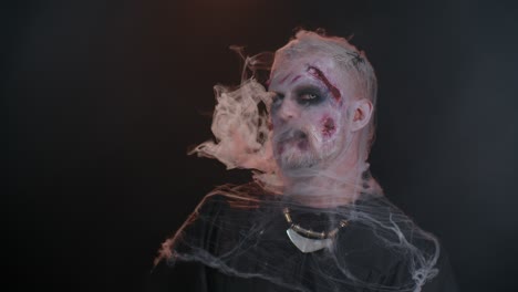 Zombie-man-with-makeup-with-wounds-scars-and-white-contact-lenses-blows-smoke-from-nose-and-mouth
