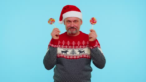 Funny-man-in-red-New-Year-sweater-holding-candy-striped-lollipops-hiding-behind-them,-fooling-around