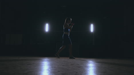 A-beautiful-woman-boxer-trains-in-a-dark-gym-and-works-out-punches-in-slow-motion.-side-view.-Steadicam-shot
