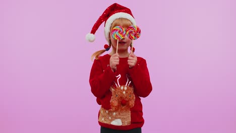 Joyful-girl-in-New-Year-sweater-holding-candy-striped-lollipops-hiding-behind-them,-fooling-around