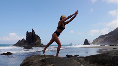 With-a-gentle-pace,-a-young-woman,-slim-and-graceful,-practices-yoga-on-a-seaside-rock-in-slow-motion
