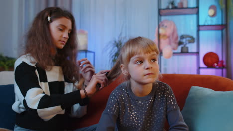 Teenage-and-little-sisters-child-kids-using-combs-brushing-make-hairstyle-coiffure-at-home-play-room