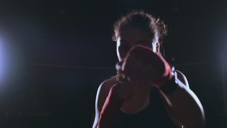 Beautiful-sexy-woman-boxer-dynamically-strikes-directly-into-the-camera-and-moving-forward-on-a-dark-background-with-a-backlight.-Steadicam-shot