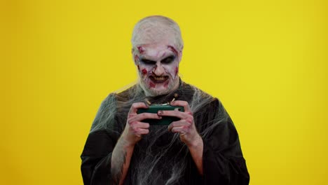 Hombre-Siniestro-Zombie-De-Halloween-Jugando-Con-Entusiasmo-Videojuegos-De-Carreras-En-El-Teléfono-Móvil
