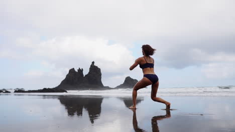 Die-Zeitlupe-Zeigt-Eine-Fitnessfrau,-Die-Am-Strand-Ihre-Beine-Streckt-Oder-Ausfallschritte-Macht,-Begleitet-Von-Einer-Sportlerin,-Die-Am-Meer-Beruhigende-Übungen-Macht