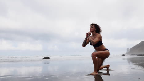 At-the-beach,-a-fitness-woman-stretches-her-legs-or-performs-lunges,-while-a-female-athlete-enjoys-calming-exercises-facing-the-sea-in-slow-motion