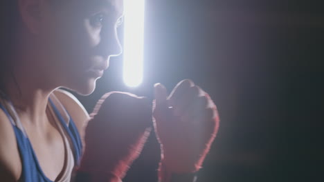 A-beautiful-woman-boxer-trains-in-a-dark-gym-and-works-out-punches-in-slow-motion.-side-view.-Steadicam-shot