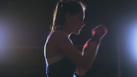 Training-a-beautiful-female-boxer-doing-punches-in-a-dark-room.-Steadicam-shot.-Preparation-for-self-defense-and-fight-in-the-ring