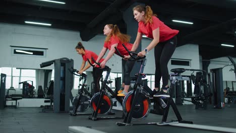 Athletic-women-group-ride-on-spin-stationary-bike-training-routine-in-gym,-weight-loss-indoors