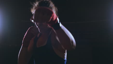 Looking-into-the-camera-a-beautiful-female-boxer-strikes-against-a-dark-background-with-a-backlit-light.-Steadicam-shot