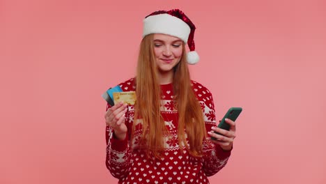 Girl-in-Christmas-sweater-using-credit-bank-card,-smartphone,-transferring-money-shopping-online